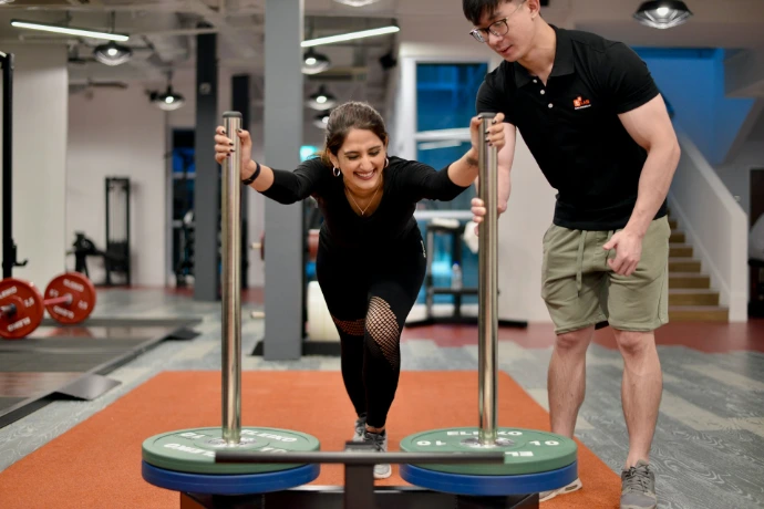 Woman performs exercise with trainer at gym.